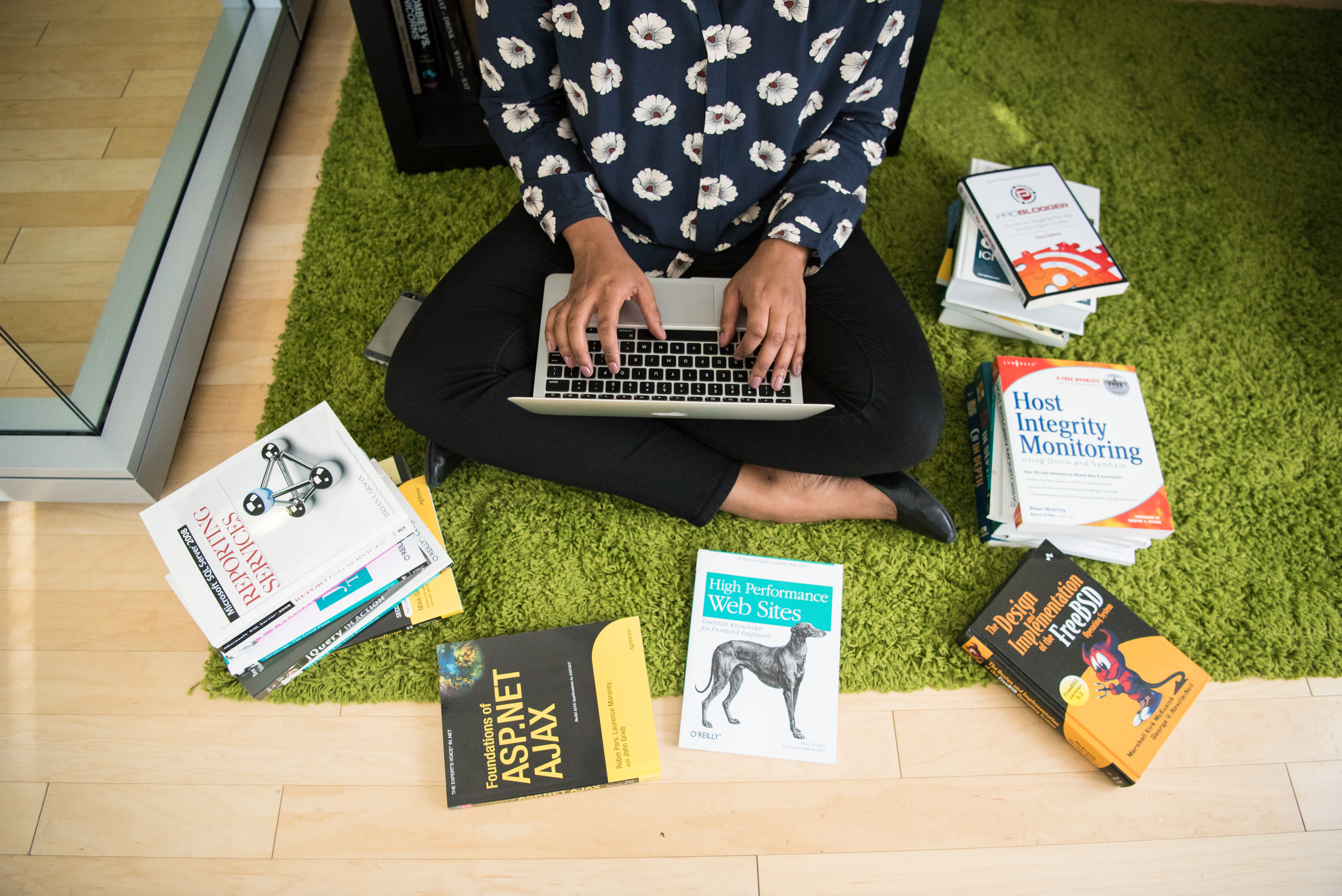 Woman types on laptop code books surround her photo by #WOCinTech Chat
