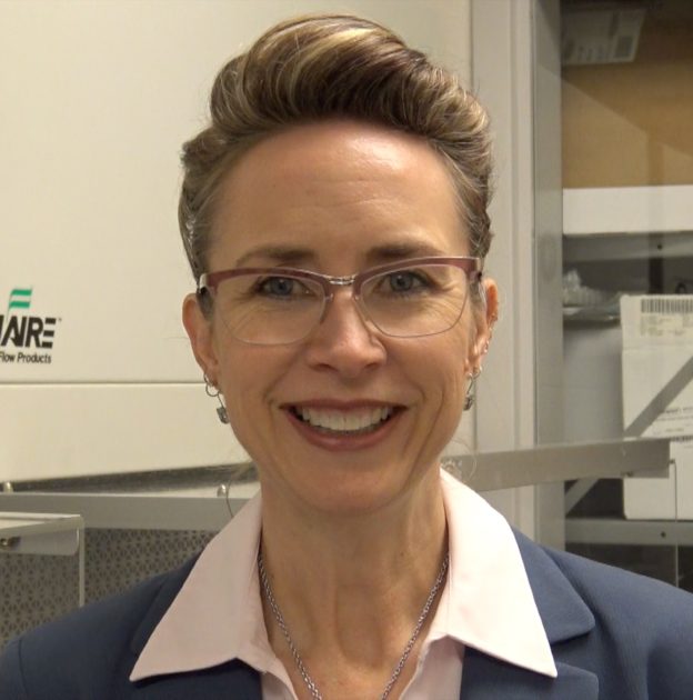 Headshot of woman with short hair, glasses, earings wearing a white shirt with a pointy collar and a blazer.